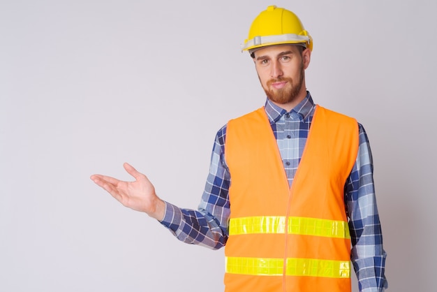 Studio shot of young bearded man construction worker against white