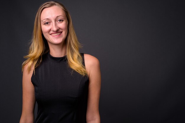 Studio shot of young beautiful businesswoman with straight blond hair against gray