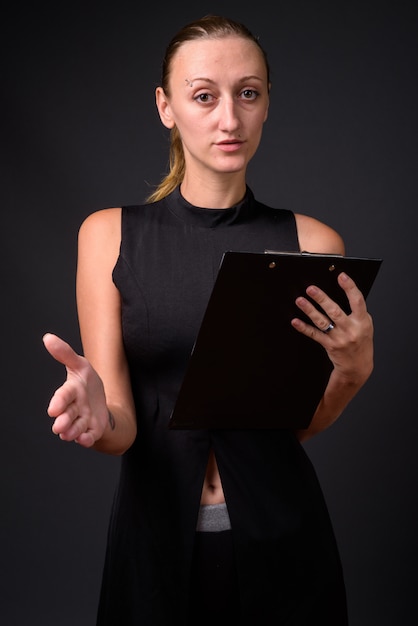 Studio shot di giovane bella imprenditrice con capelli biondi dritti contro il grigio