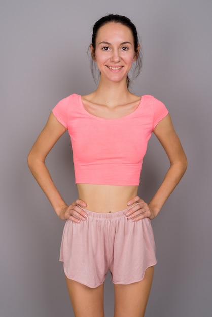 Studio shot di giovane bella donna pronta per la palestra sorridendo e guardando felice contro il grigio