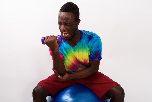 Studio shot of young black African fitness man sitting on exerci