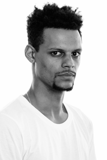 Studio shot of young handsome bearded African man with afro hair isolated against white background in black and white