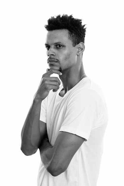 Studio shot of young handsome bearded African man with afro hair isolated against white background in black and white