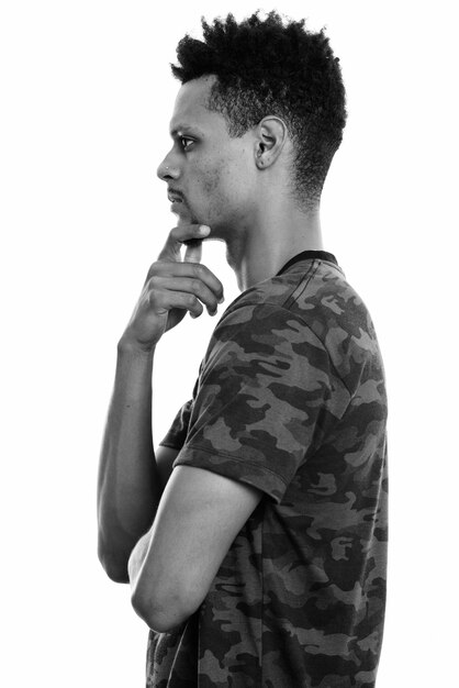 Studio shot of young handsome bearded African man with afro hair isolated against white background in black and white