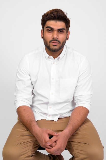 Studio shot of young handsome bearded Indian man against white