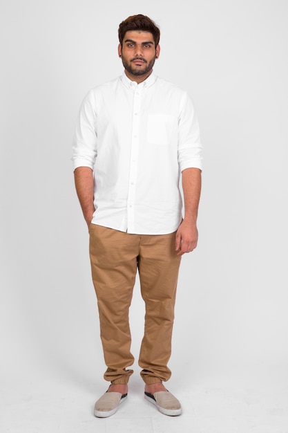 Studio shot of young handsome bearded Indian man against white