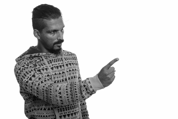 Studio shot of young handsome bearded Indian man wearing hoodie against white in black and white