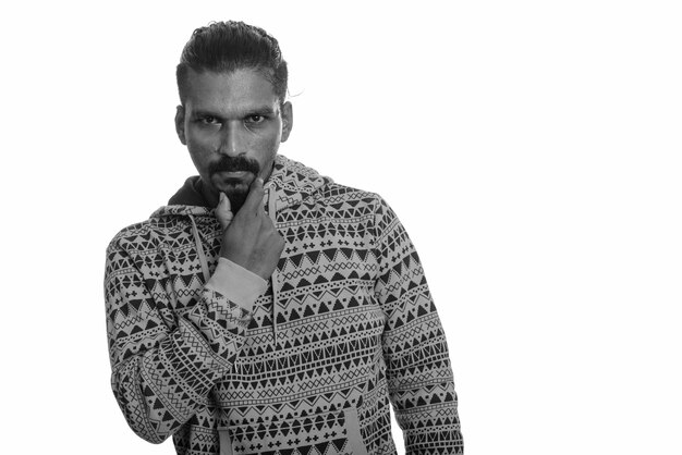 Studio shot of young handsome bearded Indian man wearing hoodie against white in black and white