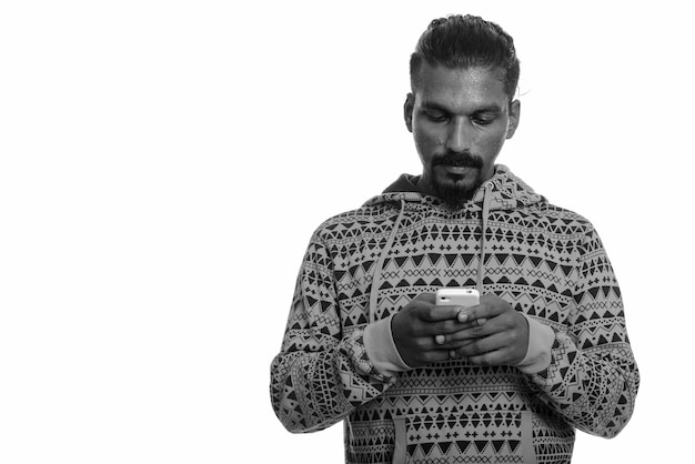 Studio shot of young handsome bearded Indian man wearing hoodie against white in black and white