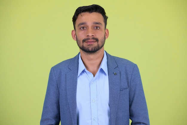 Studio shot of young handsome bearded Persian businessman in suit against chroma key with green background