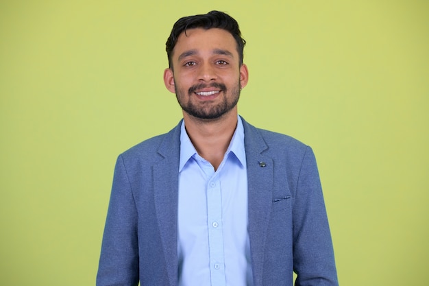 Studio shot of young handsome bearded persian businessman in suit against chroma key with green background