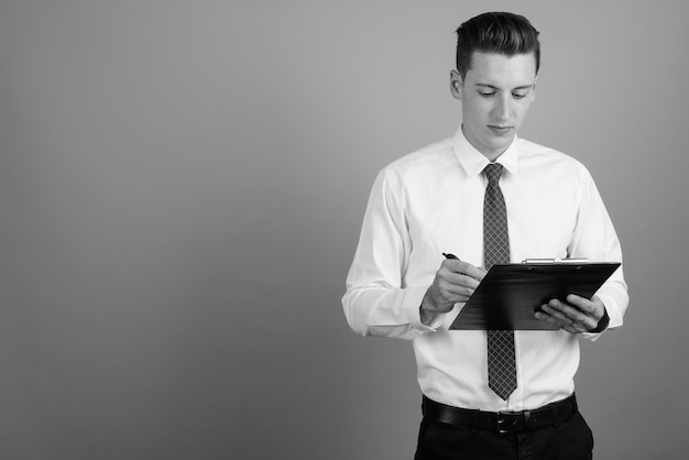 Studio shot of young handsome businessman wearing shirt and tie against gray background in black and white