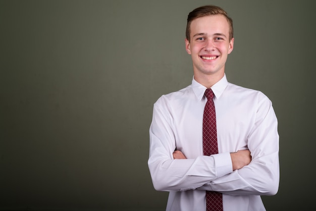 Studio shot of young handsome businessman with blond hair against colored background