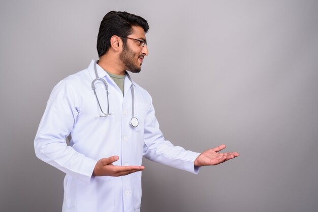 Foto studio shot di giovane bel uomo indiano medico contro il grigio