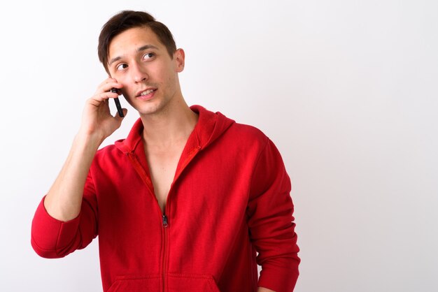 Studio shot of young handsome man thinking while talking on mobi