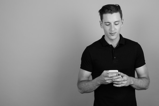 Studio shot of young handsome man using mobile phone against gray background in black and white