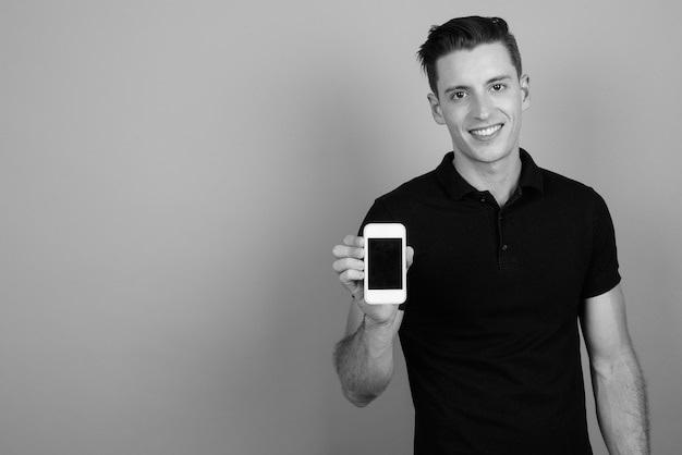 Studio shot of young handsome man using mobile phone against gray background in black and white