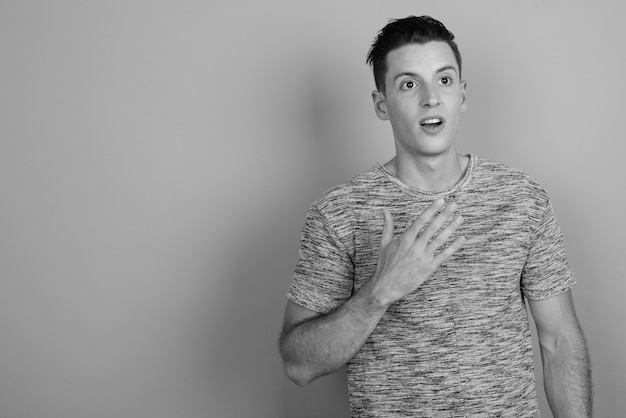 Studio shot of young handsome man wearing gray shirt against gray background in black and white