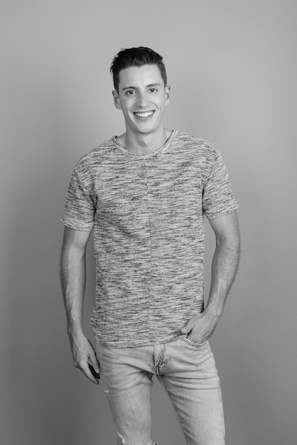 Studio shot of young handsome man wearing gray shirt against gray background in black and white