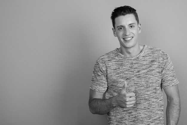 Studio shot of young handsome man wearing gray shirt against gray background in black and white