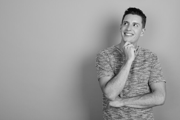 Studio shot of young handsome man wearing gray shirt against gray background in black and white