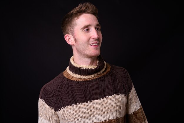 Studio shot of young handsome man with turtleneck sweater ready for winter against black background