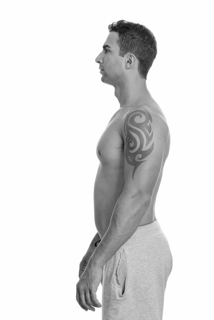 Studio shot of young handsome muscular Persian man shirtless isolated against white background in black and white