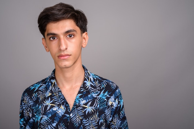 Studio shot of young handsome Persian teenage boy wearing Hawaiian shirt against gray background