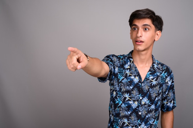 Studio shot of young handsome Persian teenage boy wearing Hawaiian shirt against gray background