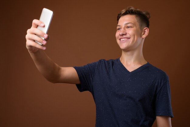 Studio shot of young handsome teenage boy against brown backgrou