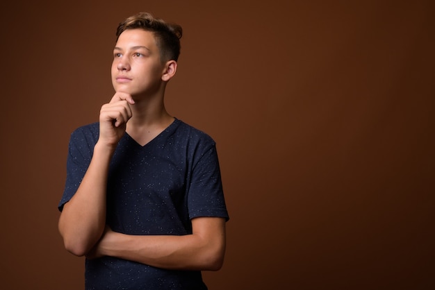 Studio shot of young handsome teenage boy against brown backgrou