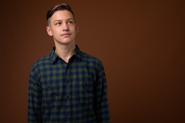 Studio shot of young handsome teenage boy against brown backgrou