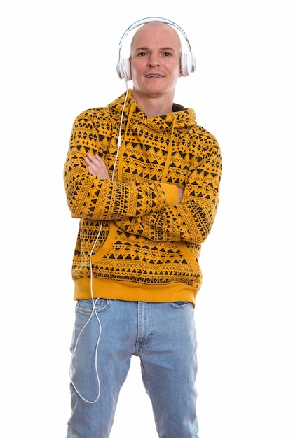 Studio shot of young happy bald man smiling and standing while listening to music