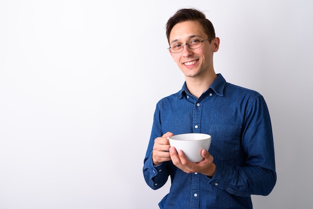 若い幸せな男の笑顔とコーヒーカップwhを保持しているスタジオショット
