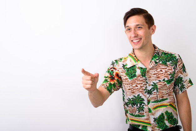 Studio shot of young happy tourist man smiling while pointing at