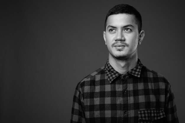 Studio shot of young multi ethnic Asian man wearing checkered shirt against gray wall in black and white