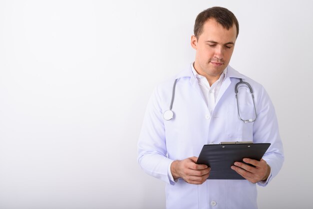 Studio shot of young muscular man doctor reading on clipboard ag