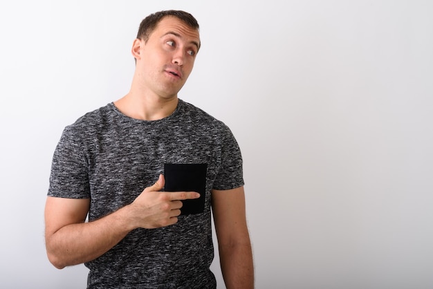 Studio shot of young muscular man thinking while pointing to the