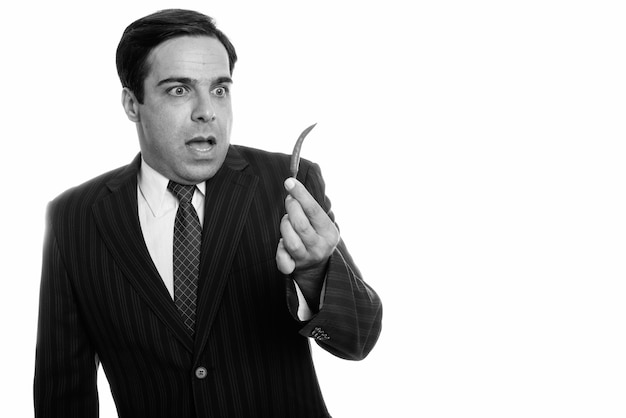 Studio shot of young Persian businessman holding red chili pepper while looking shocked isolated