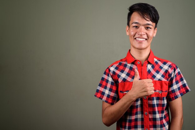 Studio shot of young teenage Indian man wearing red checkered shirt against colored