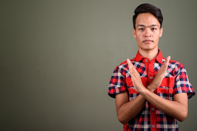 Studio shot of young teenage Indian man wearing red checkered shirt against colored