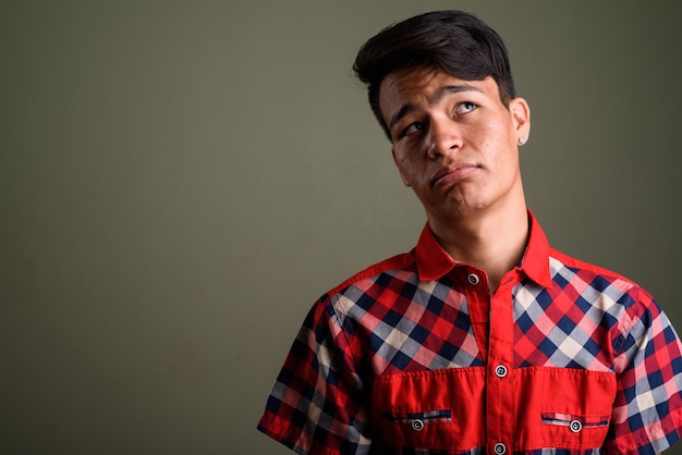 Studio shot of young teenage man wearing red checkered shirt against colored