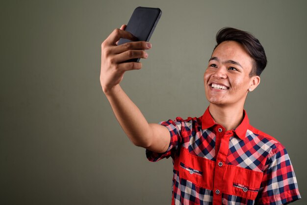 Studio shot of young teenage man wearing red checkered shirt against colored