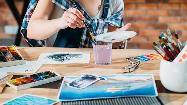 Studio werkplek. Kunstenaar aan het werk. Schilder doet aquarel. Schetsboek en paletbenodigdheden in de buurt.