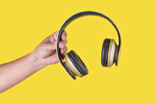 Studiofoto met gele achtergrond van een hand die een bruine draadloze hoofdtelefoon vasthoudt