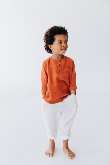 Studiofoto van een kleine jongen met een donkere huidskleur, gekleed in comfortabele linnen kleding