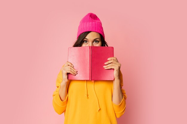 Studiofoto van gelukkige schattige student met notitieboekjes en oortelefoons die zich op roze bevinden.