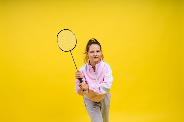 Studiofoto van volledige lengte van een tienjarig meisje dat badmintonracket vasthoudt en geïsoleerd op geel