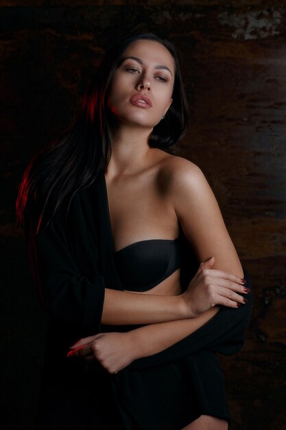 Studioportret van een jong schattig model in zwarte lingerie, poserend met rood licht