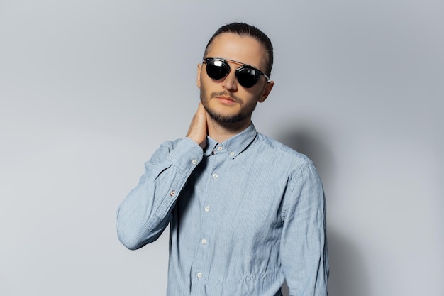 Studioportret van een jonge man met een zonnebril en een blauw shirt op een witte achtergrond